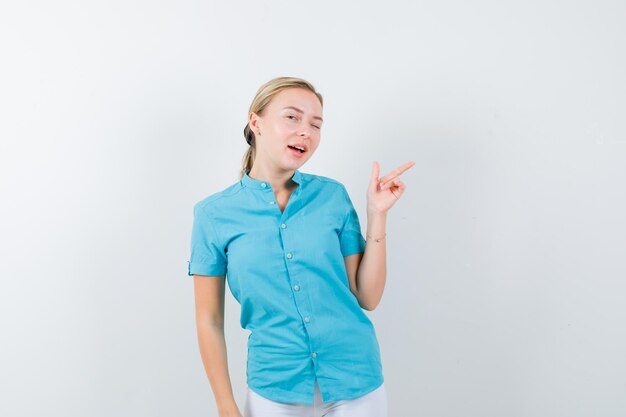 Bezpłatne zdjęcie blond kobieta wskazująca w prawo w niebieskiej bluzce i patrząca wesoło