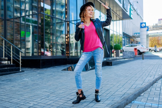 blond krótkowłosa kobieta spacerująca po ulicach dużego nowoczesnego miasta. Modny strój miejski. Niezwykłe różowe okulary przeciwsłoneczne.