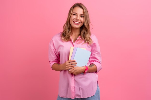 Blond ładna kobieta w różowej koszuli uśmiecha się trzymając zeszyty