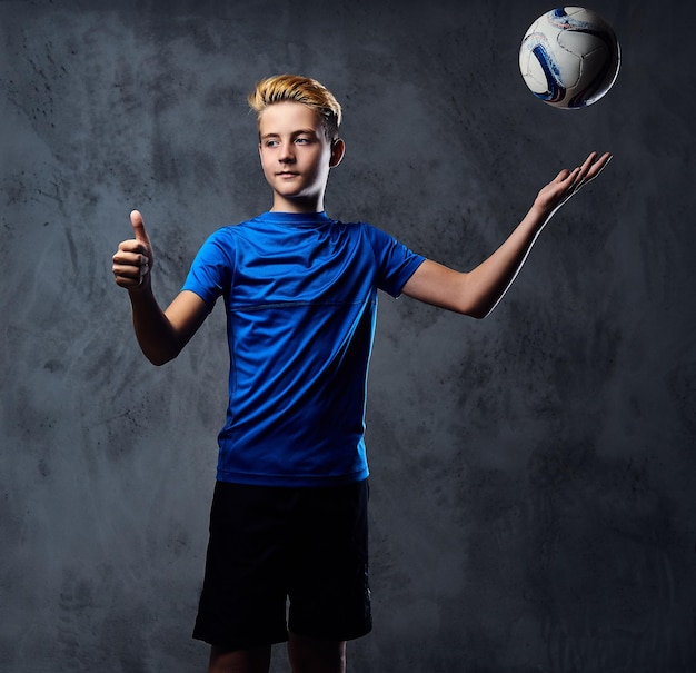 Blond nastolatka, piłkarz ubrany w niebieski mundur, bawi się piłką.