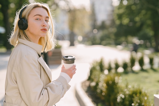 Blondynka chodzi w lecie miasta z filiżanką kawy