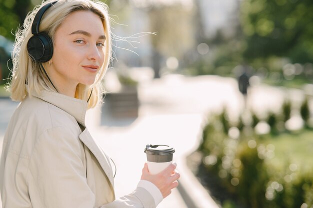 Blondynka chodzi w lecie miasta z filiżanką kawy