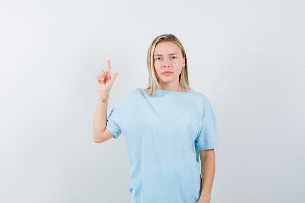 Blondynka pokazuje trzymanie na minutowym geście w niebieskiej koszulce i wygląda poważnie, widok z przodu.