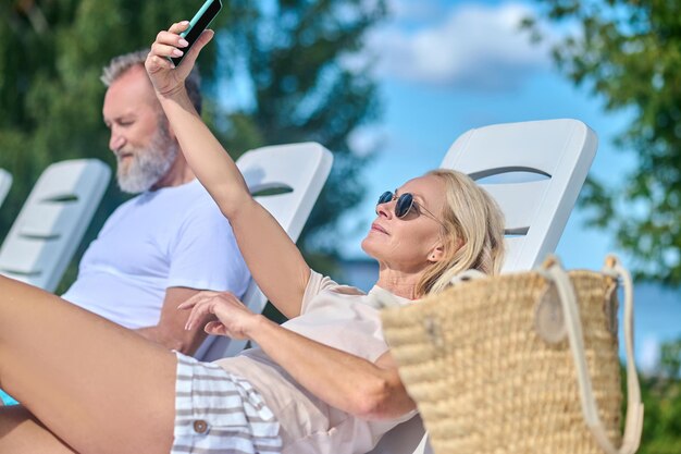 Blondynka siedzi na szezlongu i robi selfie