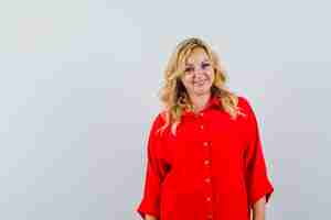 Bezpłatne zdjęcie blondynka stojąca prosto i pozowanie na kamery w czerwonej bluzce i patrząc szczęśliwy