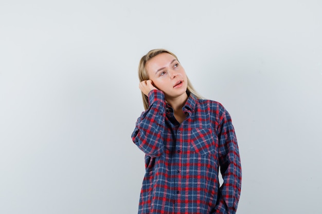 Blondynka trzymająca rękę na uchu, udająca rozmowę przez telefon w koszuli w kratkę i wyglądająca na skupioną. przedni widok.