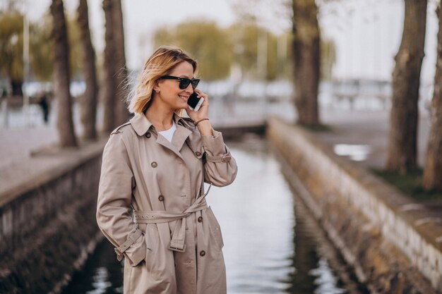 Blondynka w płaszczu na zewnątrz w parku za pomocą telefonu