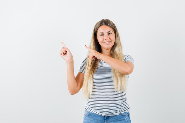 Blondynka w t-shirt, wskazując na bok i patrząc wesoło, widok z przodu.