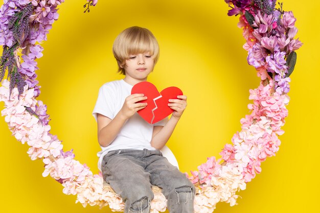 Blondynka z przodu widok ślicznego chłopca w białej koszulce o kształcie serca siedzącego na kwiatku stała na żółtej podłodze