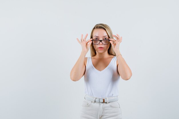 Blondynka zdejmuje okulary w podkoszulku, spodniach i wygląda rozsądnie