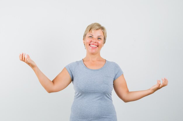 Blondynki kobieta pokazuje bezradny gest w jasnoniebieskiej koszulce i wygląda szczęśliwy, widok z przodu.