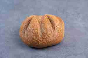 Bezpłatne zdjęcie bochenek chleba pokryty sezamem na marmurowym tle. zdjęcie wysokiej jakości
