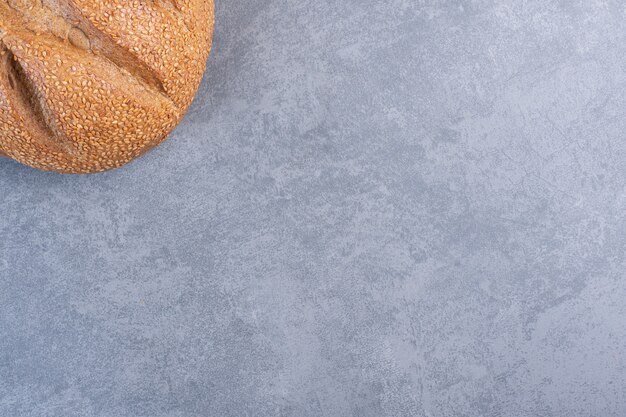 Bochenek chleba pokryty sezamem na marmurze.