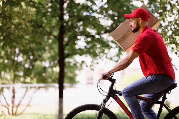 Bocznego widoku doręczeniowy mężczyzna niesie pakuneczek na rowerze