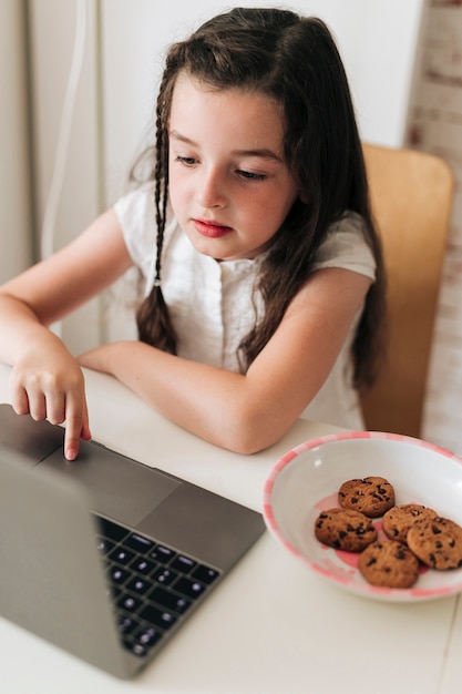 Bocznego widoku dziewczyna z ciastkami patrzeje laptop