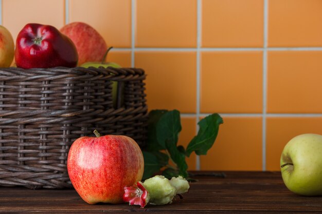 Bocznego widoku jabłka w koszu z gryźć jeden na drewnianym i pomarańczowym dachówkowym tle. poziomy