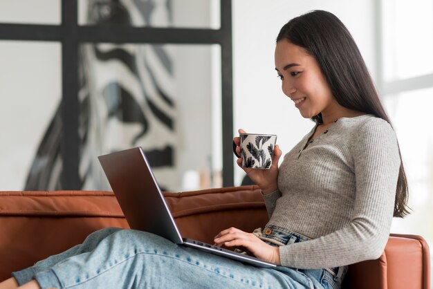 Bezpłatne zdjęcie bocznego widoku kobieta pije herbaty i używa laptop