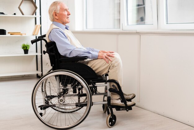 Bocznego widoku stary człowiek siedzi na wózku inwalidzkim