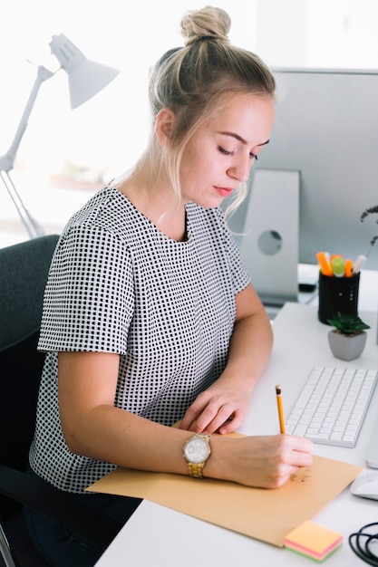 Bezpłatne zdjęcie boczny widok bizneswomanu writing na brown papierze nad białym biurkiem