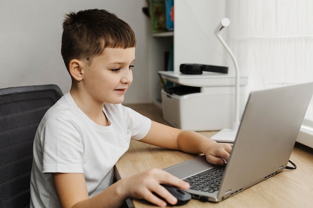 Boczny widok chłopca w domu za pomocą laptopa