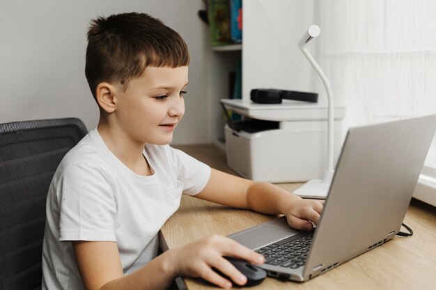 Boczny widok chłopca w domu za pomocą laptopa