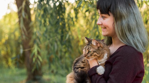 Boczny widok farbująca włosiana kobieta obejmuje jej tabby kota w lesie