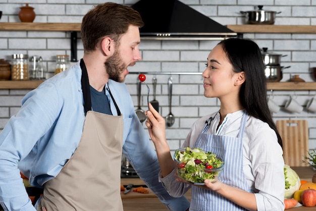 Bezpłatne zdjęcie boczny widok karmi czereśniowego pomidoru jej męża w kuchni kobieta