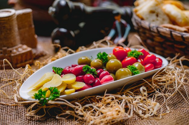 Boczny widok kiszeni warzywo pomidorów ogórki i dereń w talerzu na słomianym tle