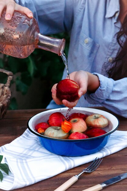 Boczny widok kobieta nalewa wodę na brzoskwini trzyma nad pucharem z świeżymi jabłkami