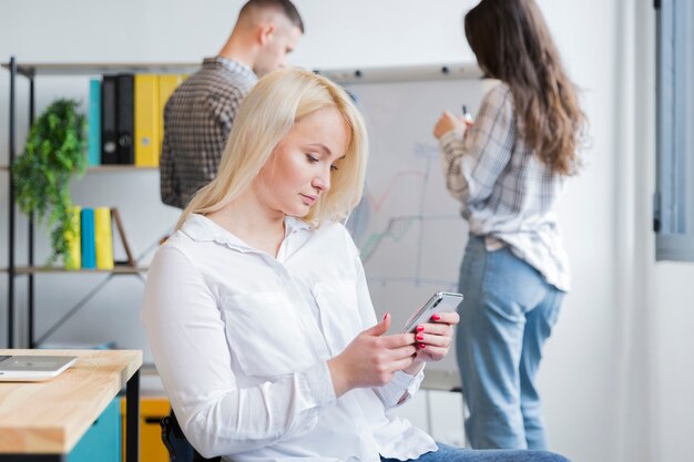 Boczny widok kobieta patrzeje telefon w biurze na wózku inwalidzkim