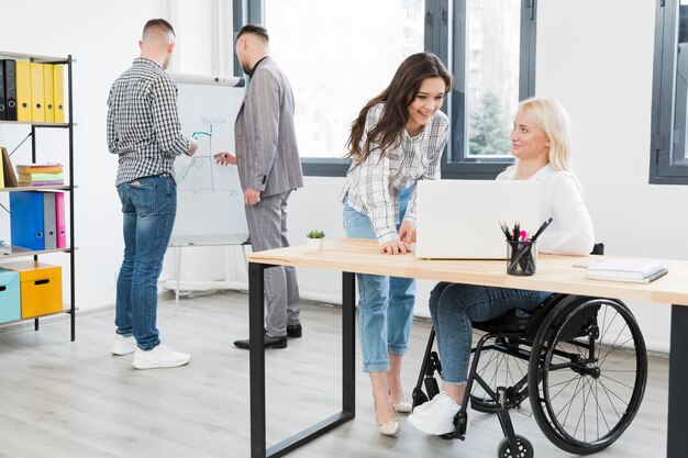 Boczny widok kobieta rozmawia z żeńskim coworker przy biurem na wózku inwalidzkim