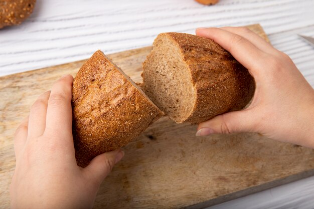 Boczny widok kobieta wręcza mienia baguette ciie w połówce na drewnianej powierzchni i tle