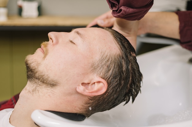 Boczny widok mężczyzna płuczkowy włosy przy fryzjera męskiego sklepem