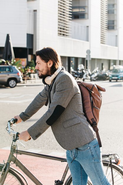 Boczny widok mężczyzna przewożenia plecaka pozycja z jego bicyklem na drodze