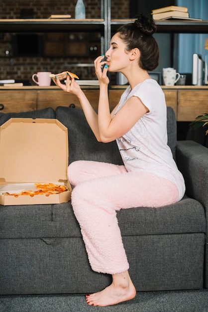 Bezpłatne zdjęcie boczny widok młodej kobiety obsiadanie na kanapy łasowania pizzy