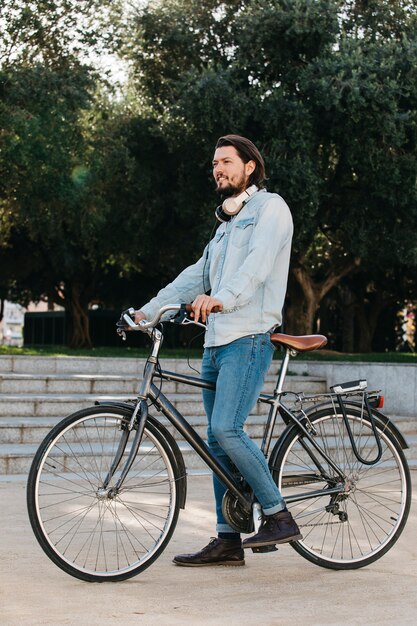 Boczny widok młody człowiek pozycja z bicyklem w parku