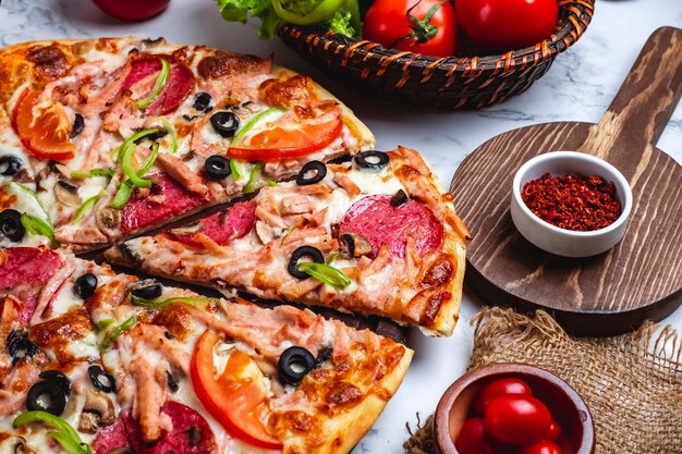 Boczny widok pizza z salami baleronu zielonymi pieprzami pomidorów czarne oliwki i ser na stole