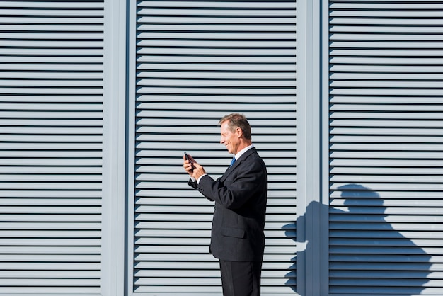 Boczny widok uśmiechnięty dojrzały biznesmen używa telefon komórkowego przy outdoors