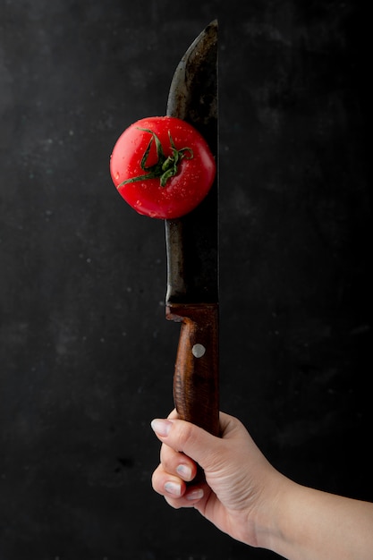 Boczny widok żeńska ręka z dojrzałym mokrym pomidorem z nożem przy czarnym tłem