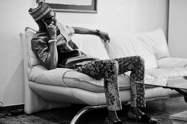 Bogaty Afrykanin siedzi na kanapie w swoim mieszkaniu Portret odnoszącego sukcesy czarnoskórego mężczyzny w pomieszczeniu