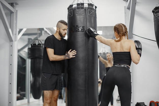 Boks kobieta. Początkujący na siłowni. Pani w czarnej sportowej odzieży. Kobieta z trenerem.