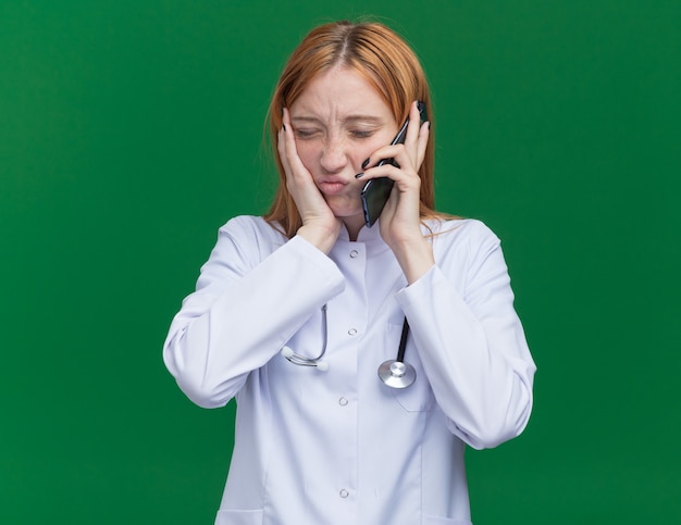 Bolący Młody żeński Imbir Lekarz Ubrany W Szatę Medyczną I Stetoskop Rozmawia Przez Telefon Trzymając Rękę Na Policzku Z Zamkniętymi Oczami Mając Ból Zęba
