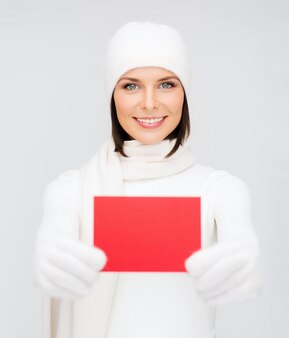Boże narodzenie, boże narodzenie, ludzie, reklama, koncepcja sprzedaży - szczęśliwa kobieta w zimowych ubraniach z pustą czerwoną kartką