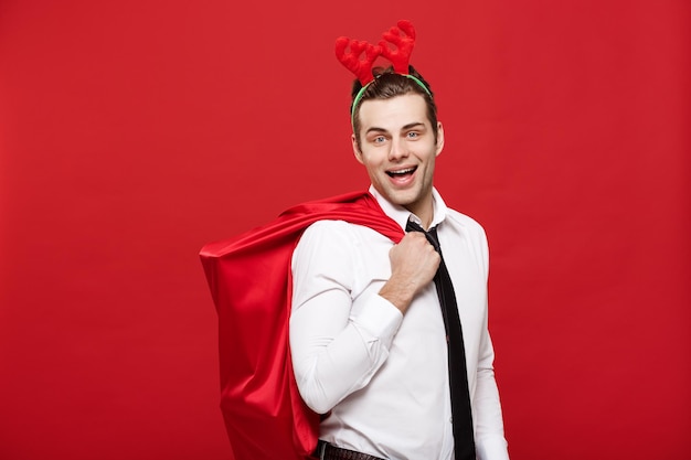 Bezpłatne zdjęcie boże narodzenie koncepcja przystojny biznesmen świętuj wesołych świąt i szczęśliwego nowego roku nosić opaskę do włosów renifera trzymającą czerwoną dużą torbę świętego mikołaja