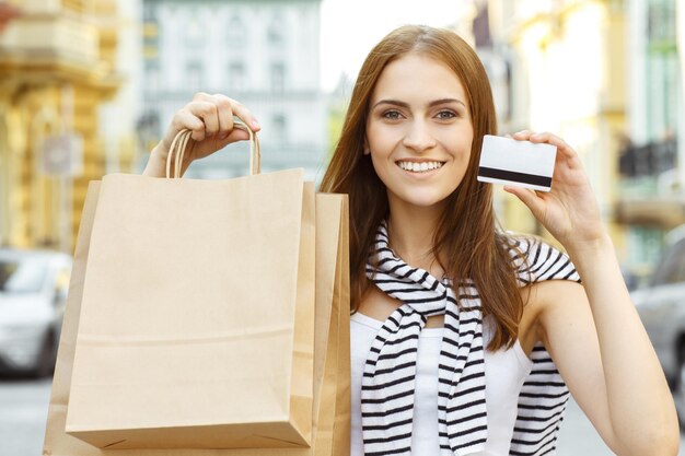 Brak limitów na zakupy Piękna szczęśliwa młoda kobieta pokazująca swoją kartę kredytową i torby po udanych zakupach