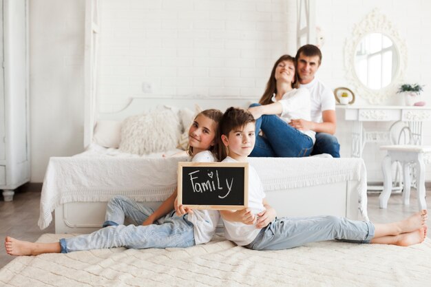 Brat i siostra trzyma łupek z tekstem rodzinnym siedząc na dywanie przed rodzicem