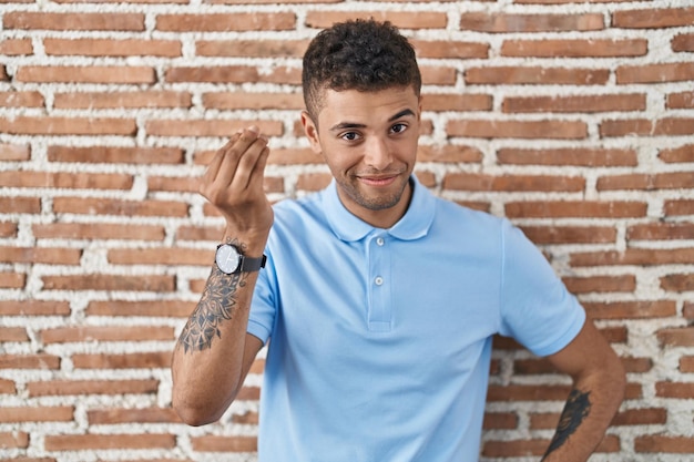 Brazylijski młody człowiek stojący nad ceglanym murem wykonujący włoski gest ręką i palcami pewny siebie