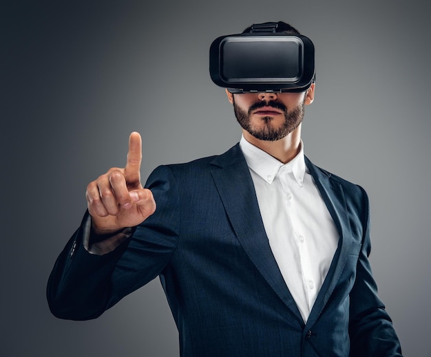 Brodaty mężczyzna ubrany w garnitur z okularami wirtualnej rzeczywistości na głowie.