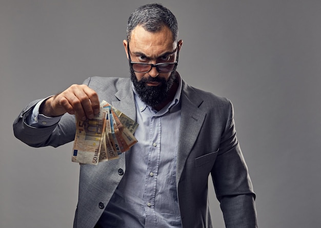 Bezpłatne zdjęcie brodaty mężczyzna ubrany w garnitur złapać banknot pieniędzy w powietrzu.