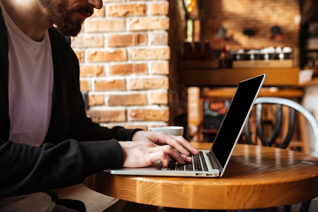 Brodaty mężczyzna używa laptop w kawiarni